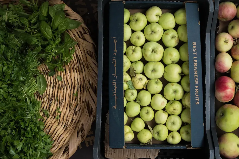 Crates of green and red apples beside baskets of fresh herbs on a market stall
