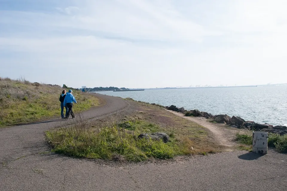 Two people walking along a paved path beside the water on a sunny day