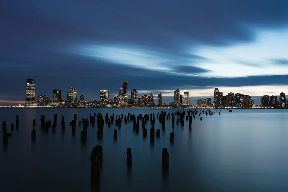 The Jersey City skyline across the Hudson River at dusk, seen from a park in New York