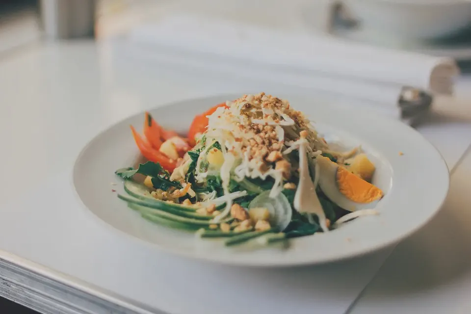 A plate of mixed salad with vegetables, egg and nuts on a white table