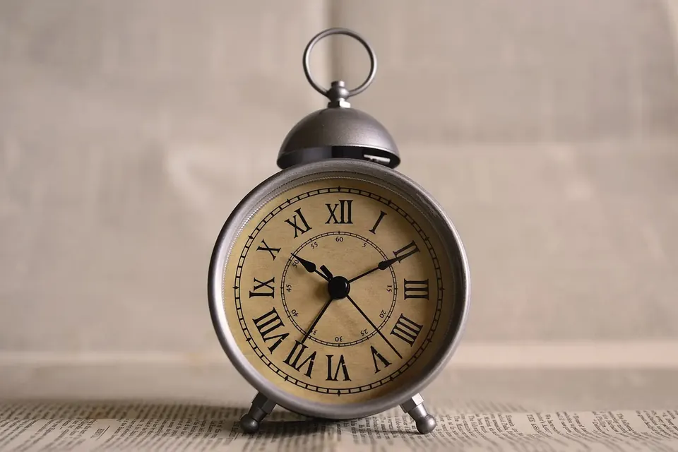 A vintage bell alarm clock with Roman numerals on a cream background