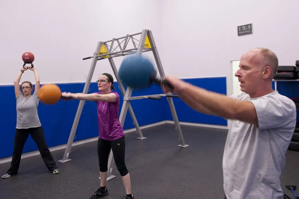 Three adults swinging kettlebells during a group class in a gym